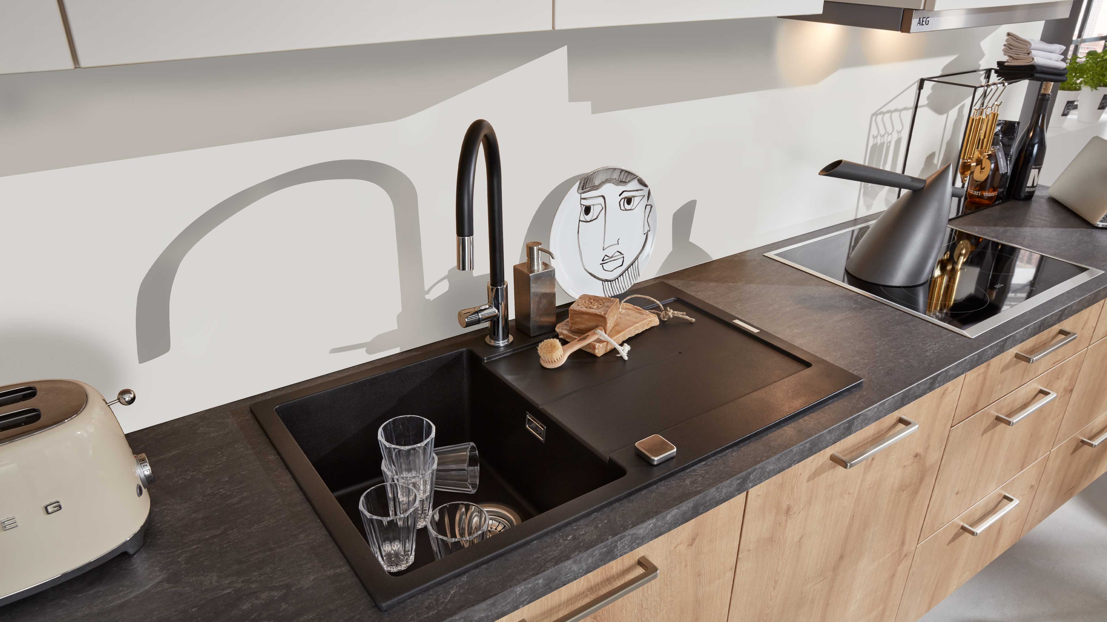 Schwarze, rechteckige Einbauspüle mit matter Oberfläche und Abdeckplatte, kombiniert mit gebogenem schwarzen Hahn auf dunkler Arbeitsplatte.